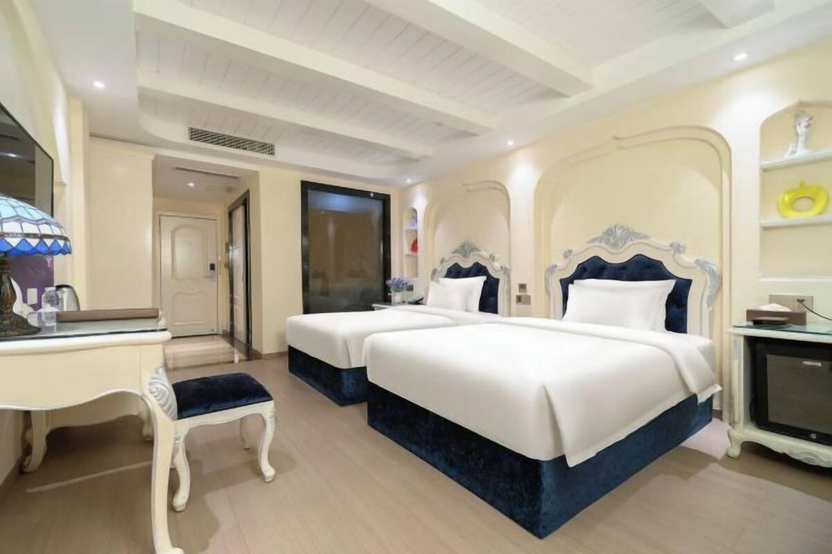 A hotel room with two beds, a desk, a chair, and a television.