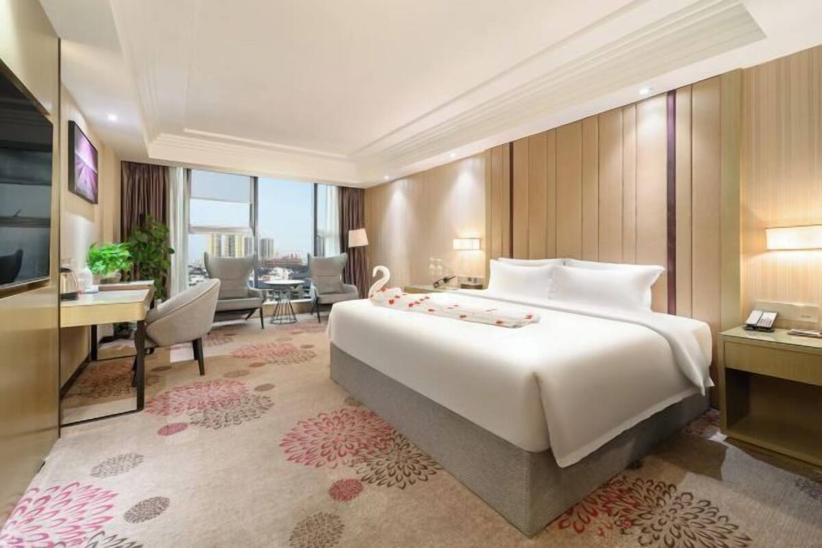 A hotel room with a large bed, a desk, a chair, and a small table.