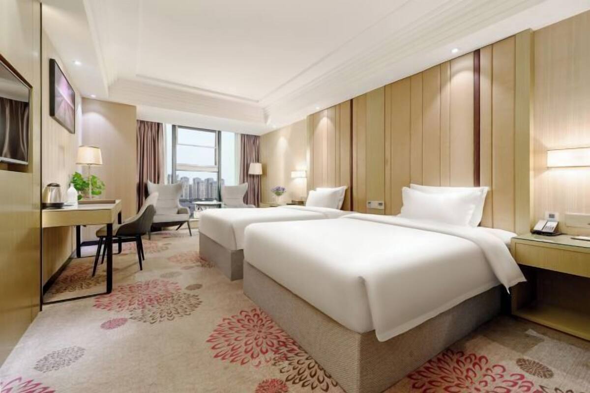 A hotel room with two beds, a desk, a chair, and a large window.