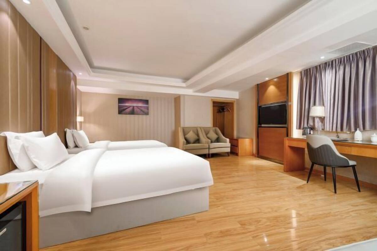 A hotel room with a large bed, a desk, a chair, a TV, and a window with curtains.