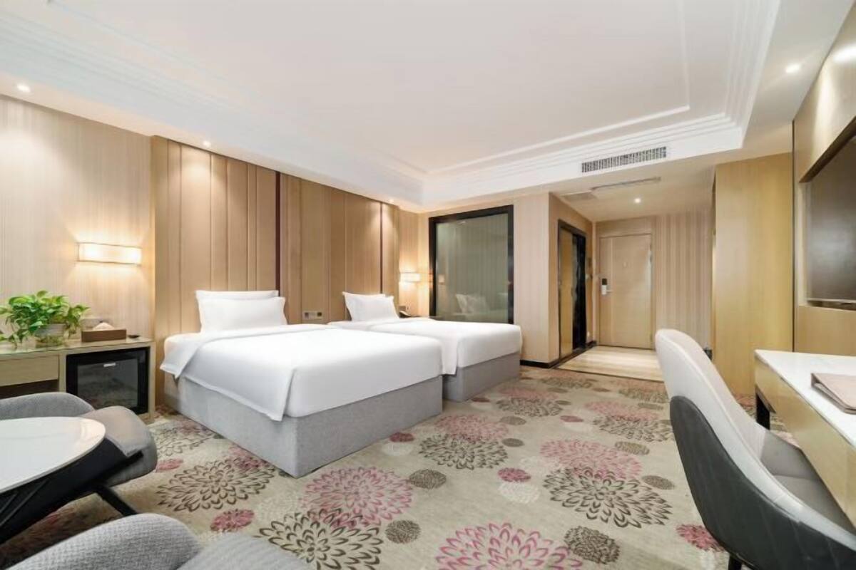 A hotel room with a double bed, a desk, a chair, a small table, a TV, and a door.