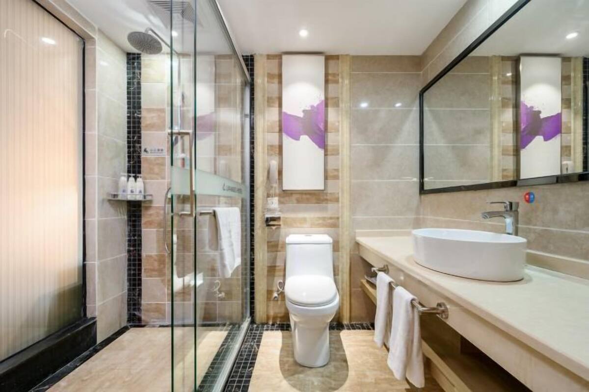 A modern bathroom with a glass-enclosed shower, a white toilet, and a large mirror above the sink.