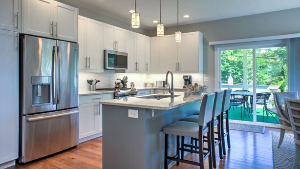 A modern kitchen with white cabinets, stainless steel appliances, a central island with bar stools, and a large window offering a view of greenery. - 4 Kings Walkable to Lake Louise. (Weaverville)