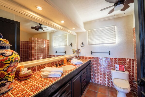 Un baño con salpicadero de azulejos, un espejo grande, un ventilador de techo y un inodoro con un cartel encima.