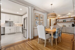 Une cuisine moderne avec des meubles blancs, une table à manger en bois et un lustre.