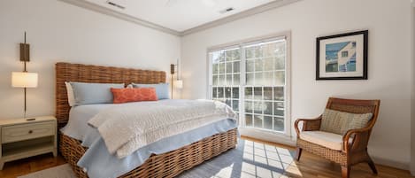 A bedroom with a large bed, a wicker chair, a window with blinds, and a ceiling fan.