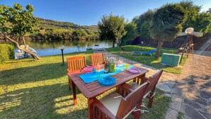 An outdoor dining area with a wooden table and chairs, set against a backdrop of a lake and greenery.