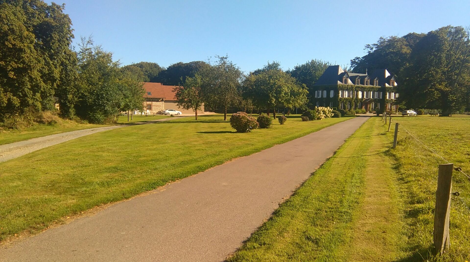 A paved pathway leading to a large building with a red roof, surrounded by green grass and trees.