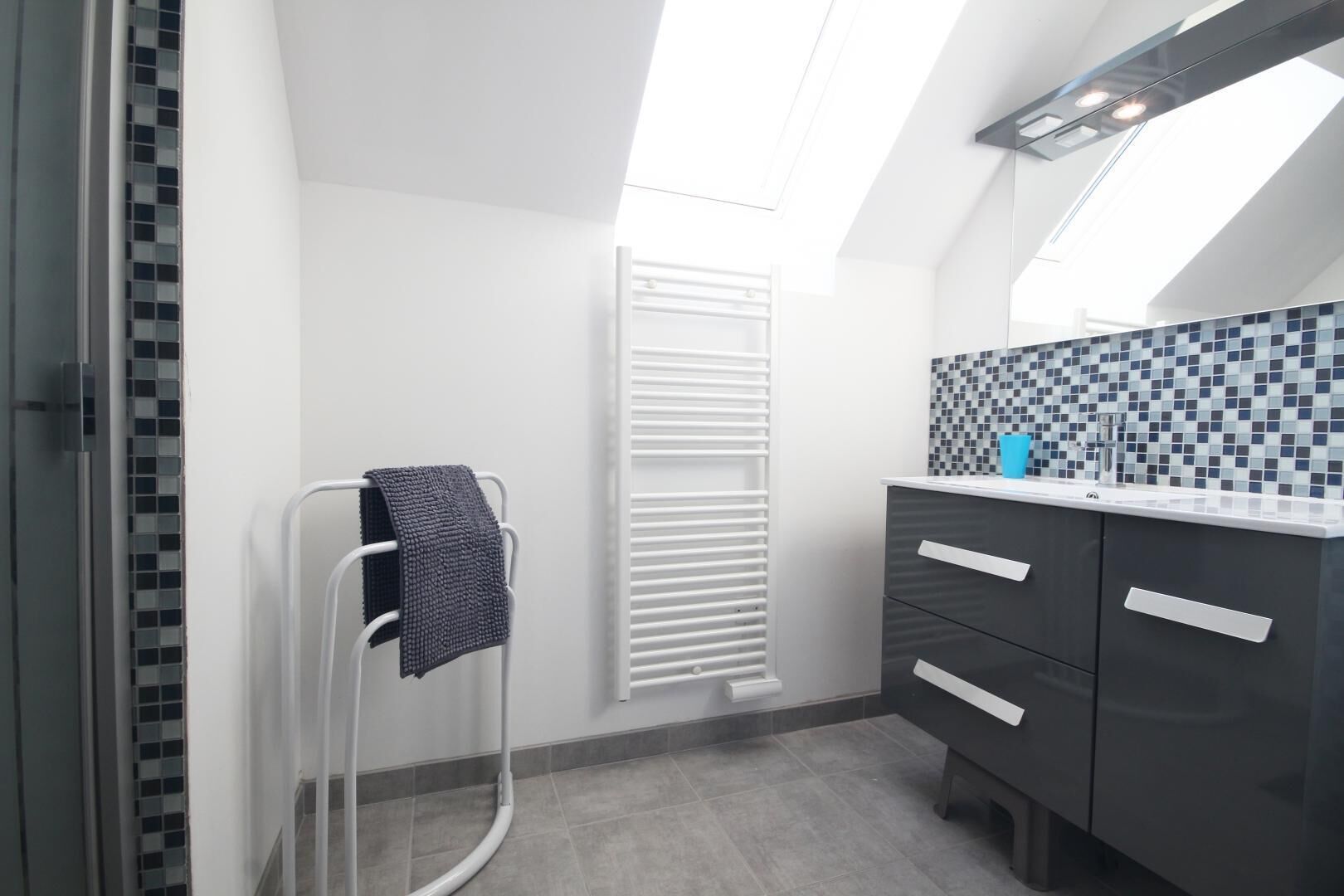 A modern bathroom with a skylight, a towel rack, a toilet, and a sink with a tiled backsplash.