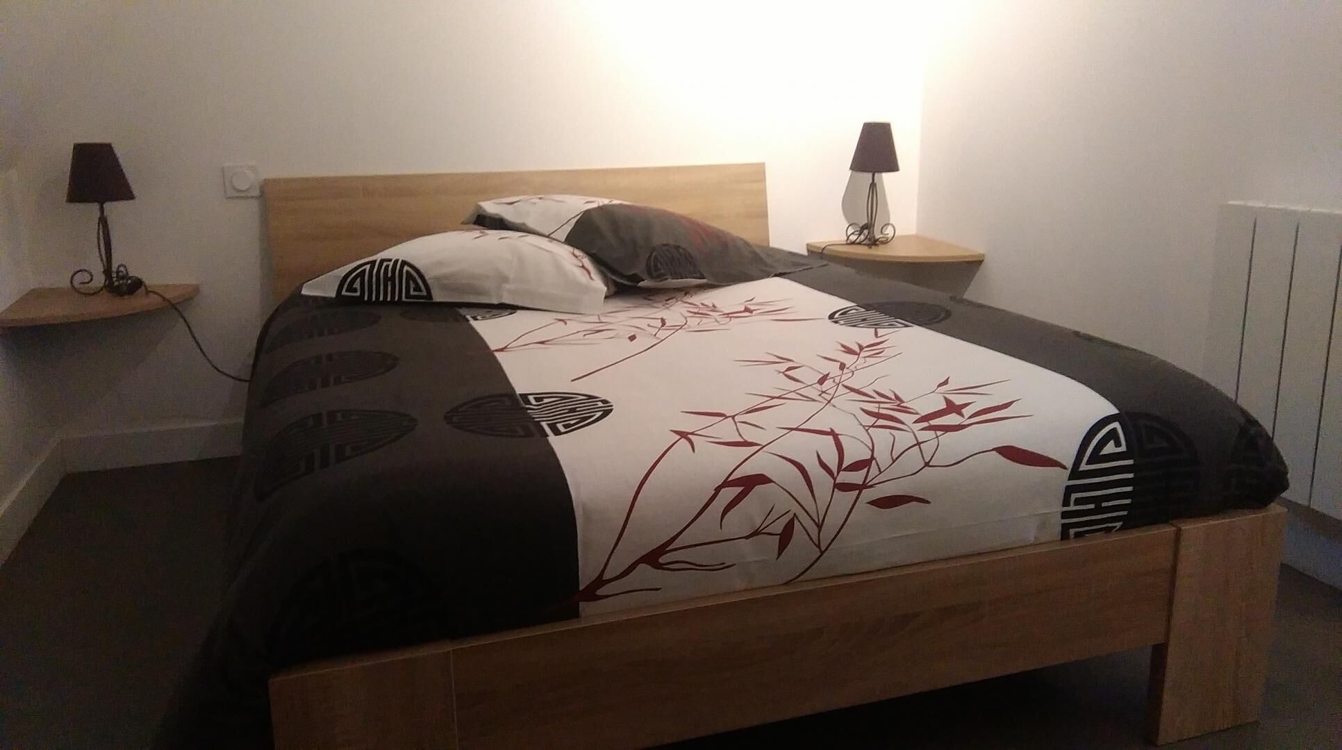 A neatly made bed with a patterned bedspread, two bedside tables with lamps, and a wooden headboard.