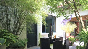 Un espace patio avec une table et des chaises en osier noir, entouré de plantes en pot et d’une clôture en bambou.