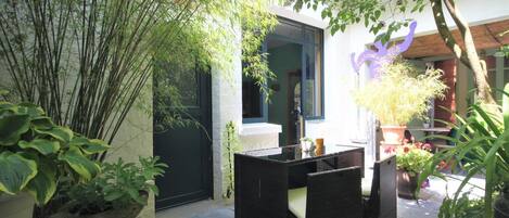 A patio area with a black wicker table and chairs, surrounded by potted plants and a bamboo fence.