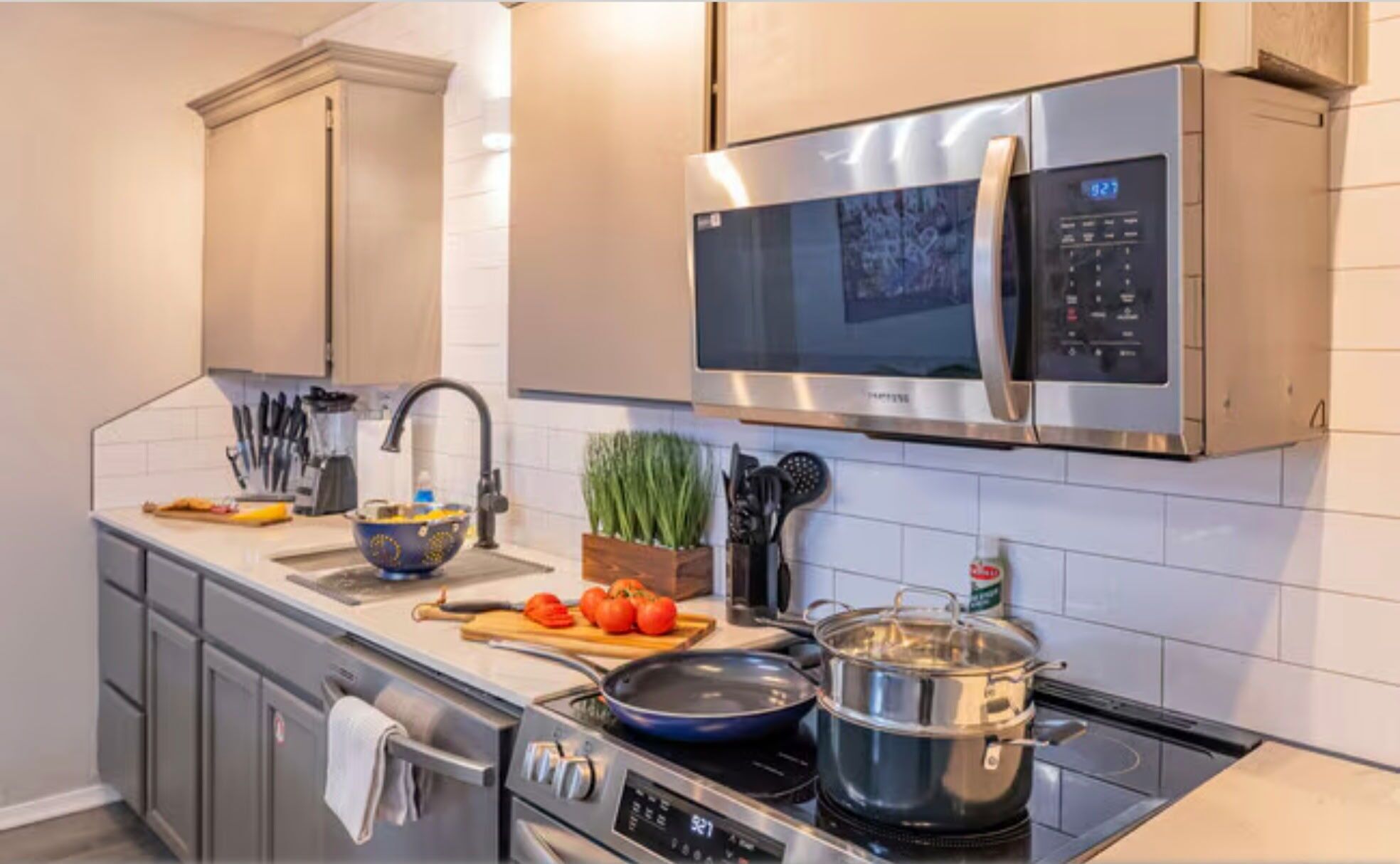 Une cuisine moderne équipée d’appareils électroménagers en acier inoxydable, notamment un four à micro-ondes, un four et une cuisinière. On y trouve un évier avec un robinet, une planche à découper avec des tomates et une casserole sur la cuisinière.