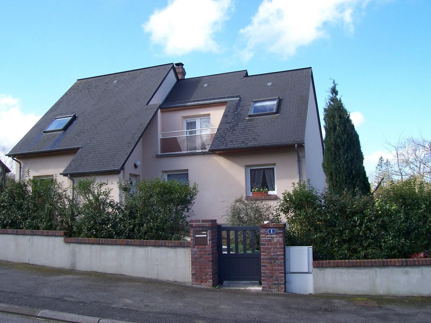 A two-story house with a sloped roof, a balcony, and a gated entrance.
