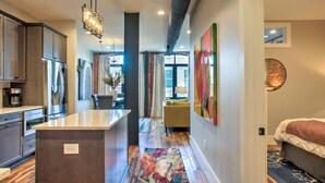 Une cuisine moderne avec un îlot central, un coin repas doté d’un canapé jaune et une chambre avec un lit et une décoration murale circulaire.