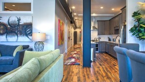 Un salon moderne avec un canapé, une table basse et un tapis, qui mène à une cuisine dotée d’un plancher et de meubles en bois.