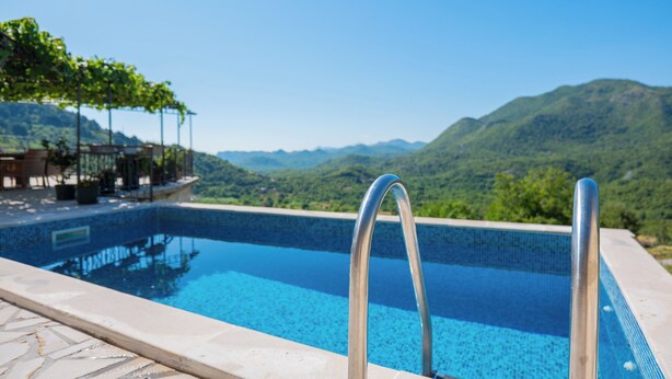 A swimming pool with metal railings, surrounded by a stone deck, and overlooking a mountainous landscape.