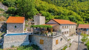 A stone building with a red-tiled roof, a pool, and a garden area with outdoor seating.