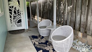 Un área de patio techada con mobiliario de ratán blanco, una puerta decorativa y una valla de madera.