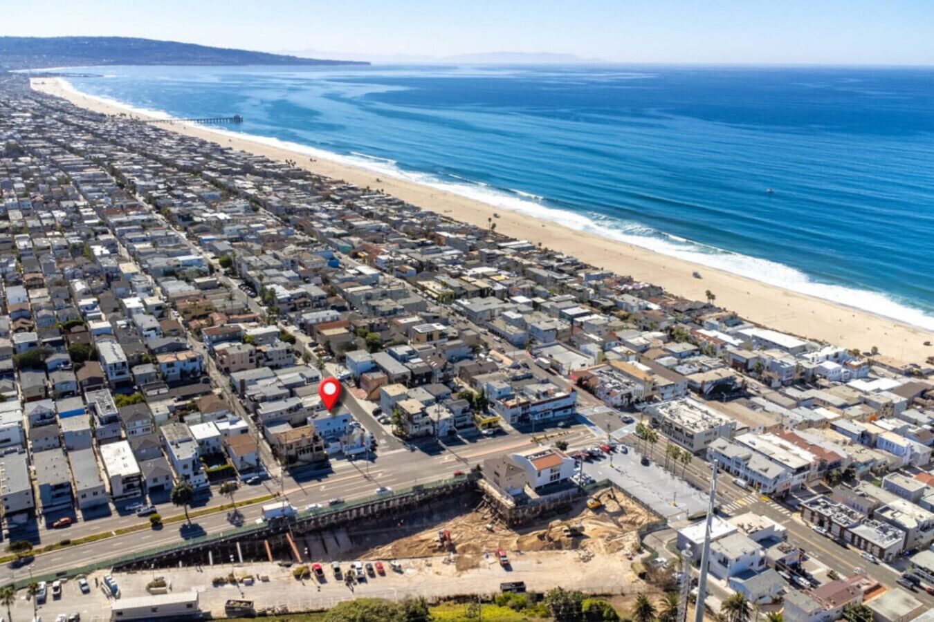 An aerial view of a coastal residential area with a beach, houses, and a road.