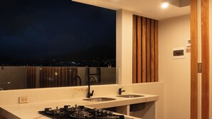 A modern kitchen with a large island, stainless steel appliances, and a view of the city at night. - Qasamarca Hotel Boutique (Cajamarca)