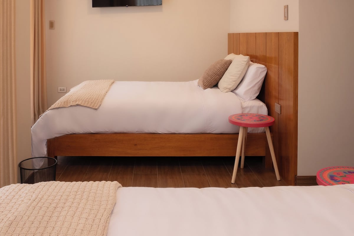 Una cama individual con cabecera de madera, una mesita de noche pequeña y un televisor montado en la pared.