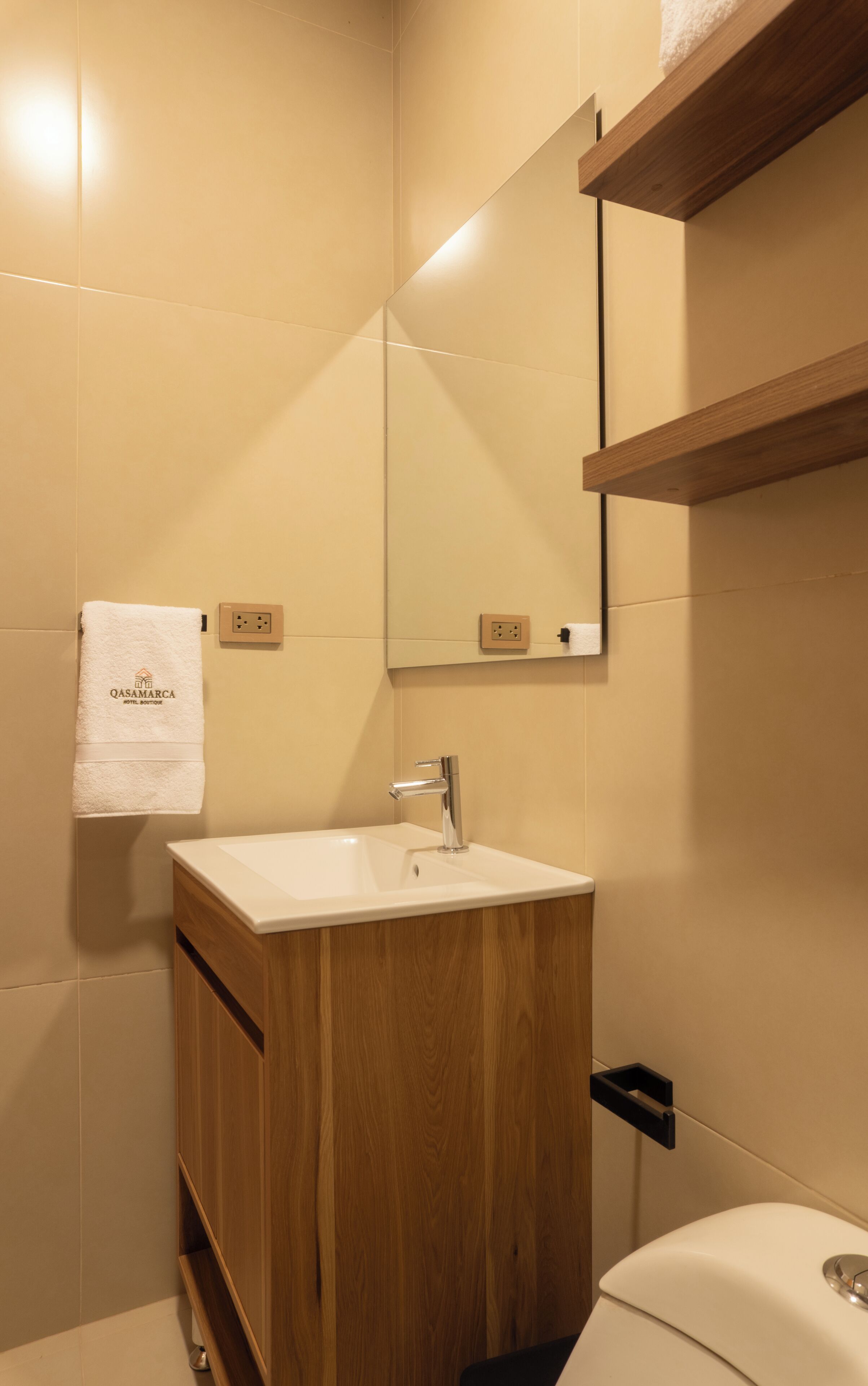 Un bany amb un moble de tocador de fusta, un lavabo blanc, un mirall i una tovallola penjada a la paret.