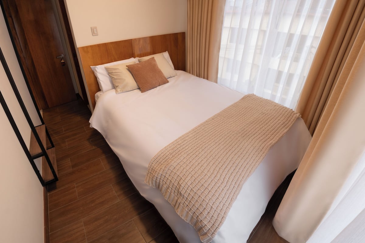 Una cama bien hecha con cabecera de madera, una manta color beige y dos almohadas.