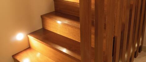Una escalera de madera con barandillas e iluminación en los peldaños, que lleva a un piso superior.