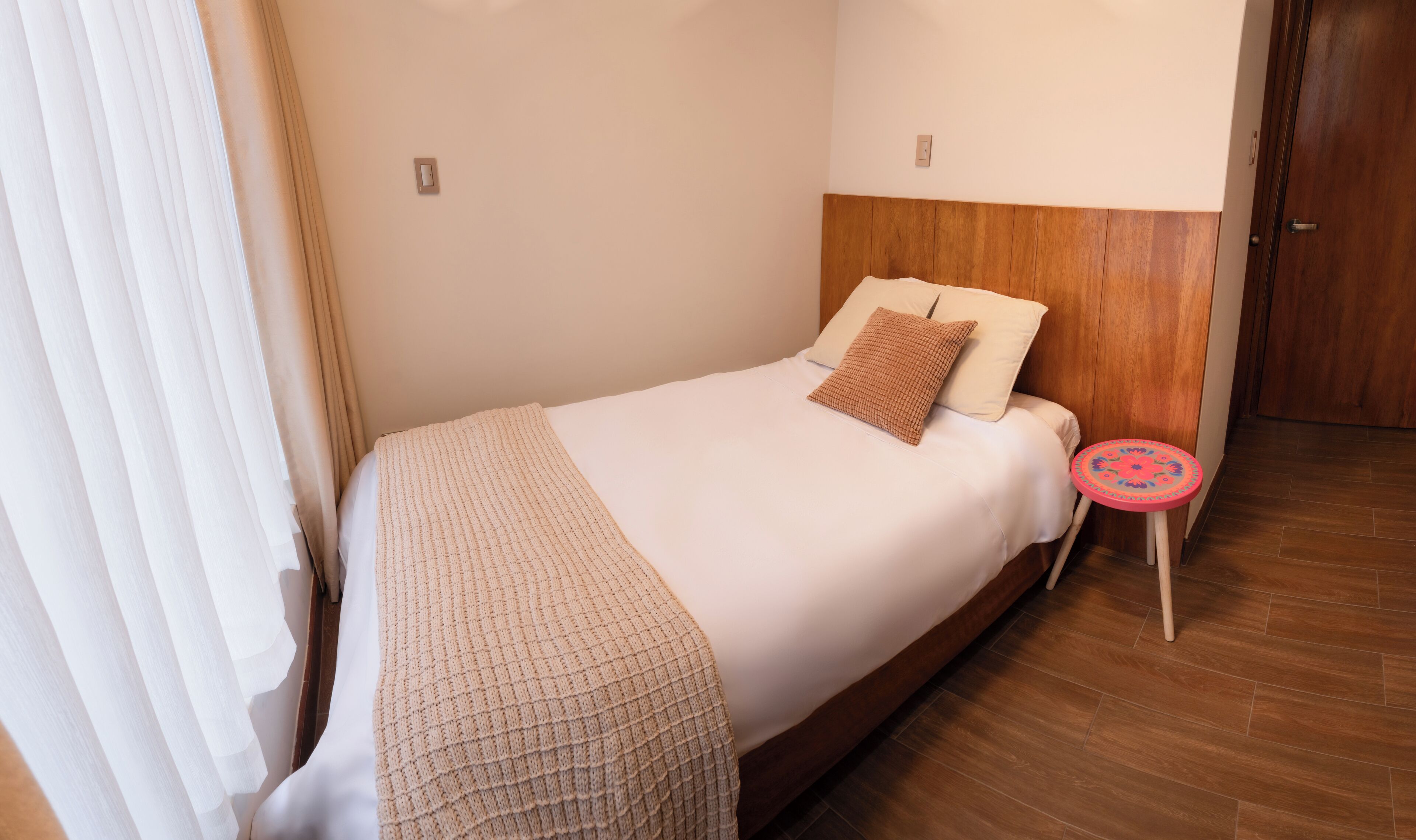 Une chambre à coucher avec un lit, une table de chevet, une tête de lit en bois et une porte.