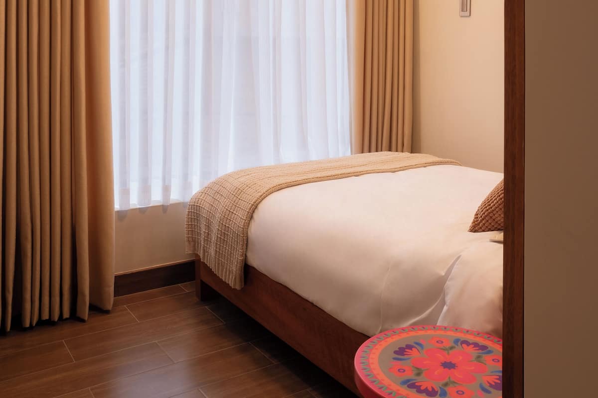 Una habitación de hotel con una cama, una pequeña mesa redonda y una ventana con cortinas.