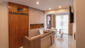 A modern reception area with a wooden reception desk, a mounted TV, and a seating area with a glass table. - Qasamarca Hotel Boutique (Cajamarca)