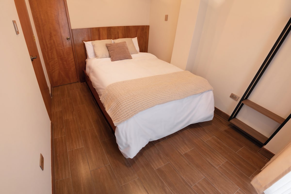 Una cama bien hecha con cabecera de madera, una colcha color beige y dos almohadas.