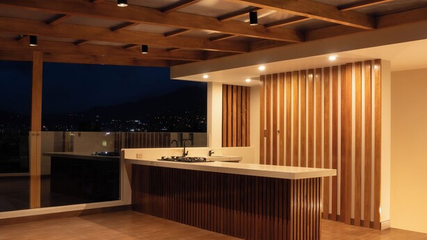 A spacious balcony with a wooden floor, a modern bar area with a sink, and a view of the city at night. - Qasamarca Hotel Boutique (Cajamarca)