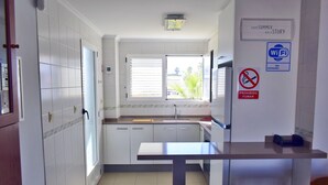 A modern kitchen with white cabinets, a countertop, and a window with blinds. - Anacasa San Fernando MET Oliva Nova AP611 (Oliva)