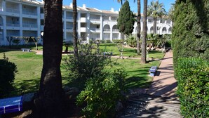 A hotel with multiple balconies, a well-maintained garden with palm trees, and a clear blue sky. - Anacasa San Fernando MET Oliva Nova AP611 (Oliva)