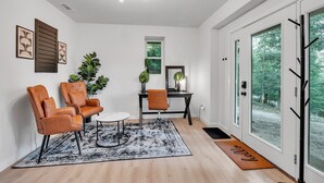 Een moderne woonkamer met twee leren fauteuils, een bijzettafeltje, een vloerkleed en een groot raam met uitzicht op bomen.