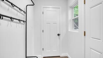 Un couloir avec une porte blanche, un porte-manteau et une fenêtre donnant sur un paysage verdoyant.
