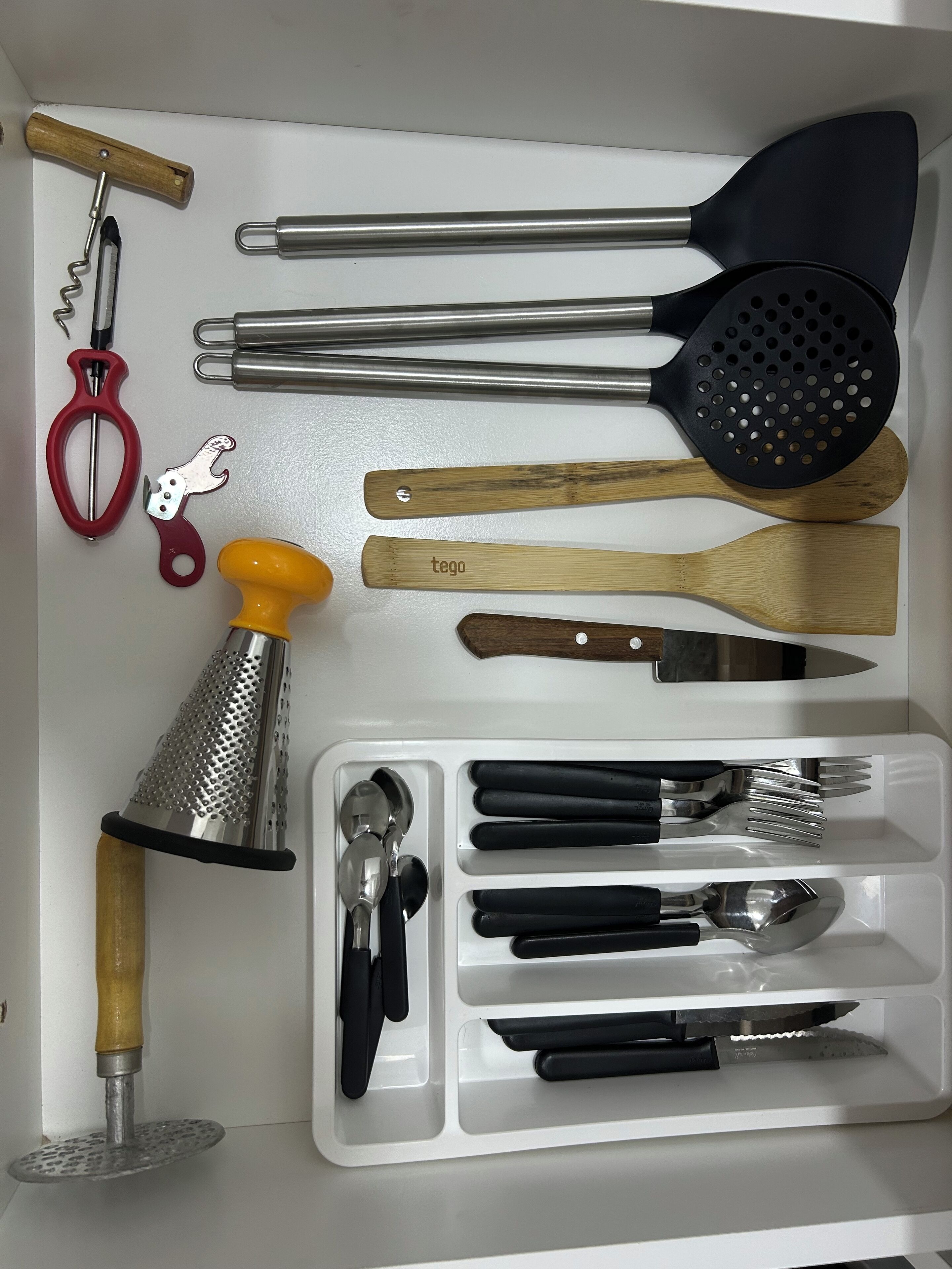 A kitchen drawer with various utensils including a grater, spatulas, tongs, and a can opener.