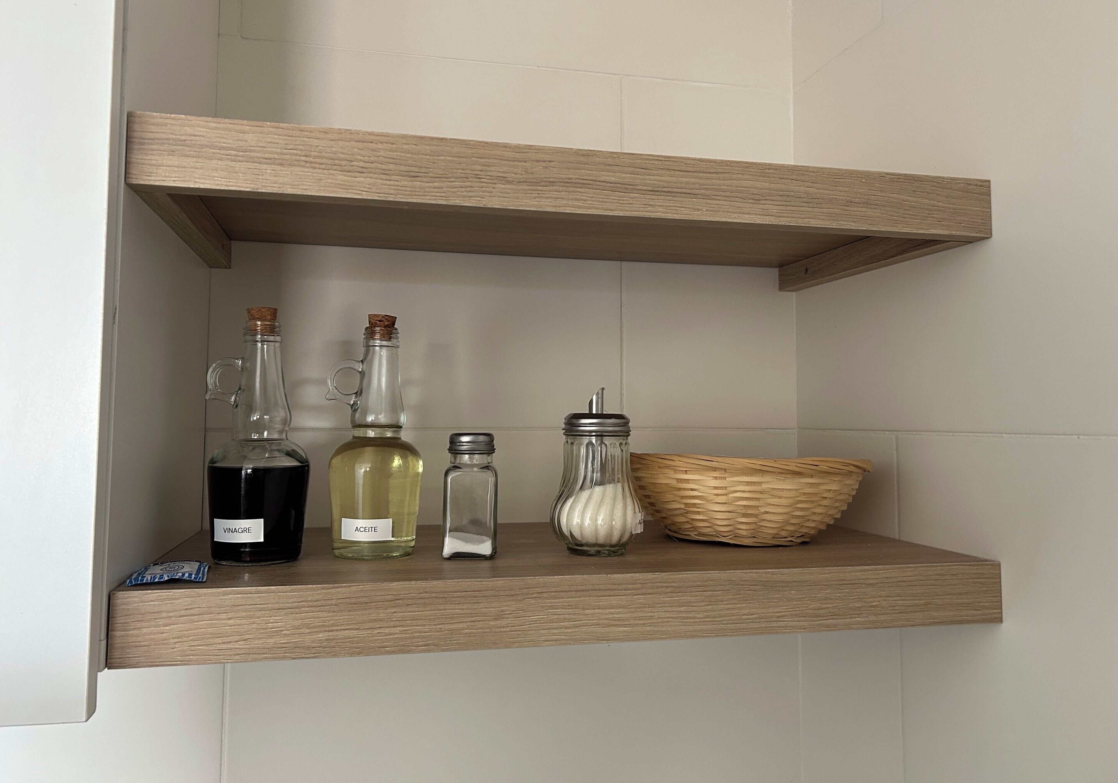 Een houten plank met vier glazen flessen, gelabeld met azijn, olie, zout en een witte substantie, en een rieten mand.