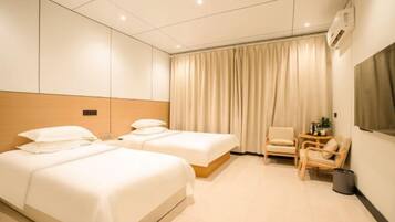 A hotel room with two beds, a chair, a small table, and a window with curtains.