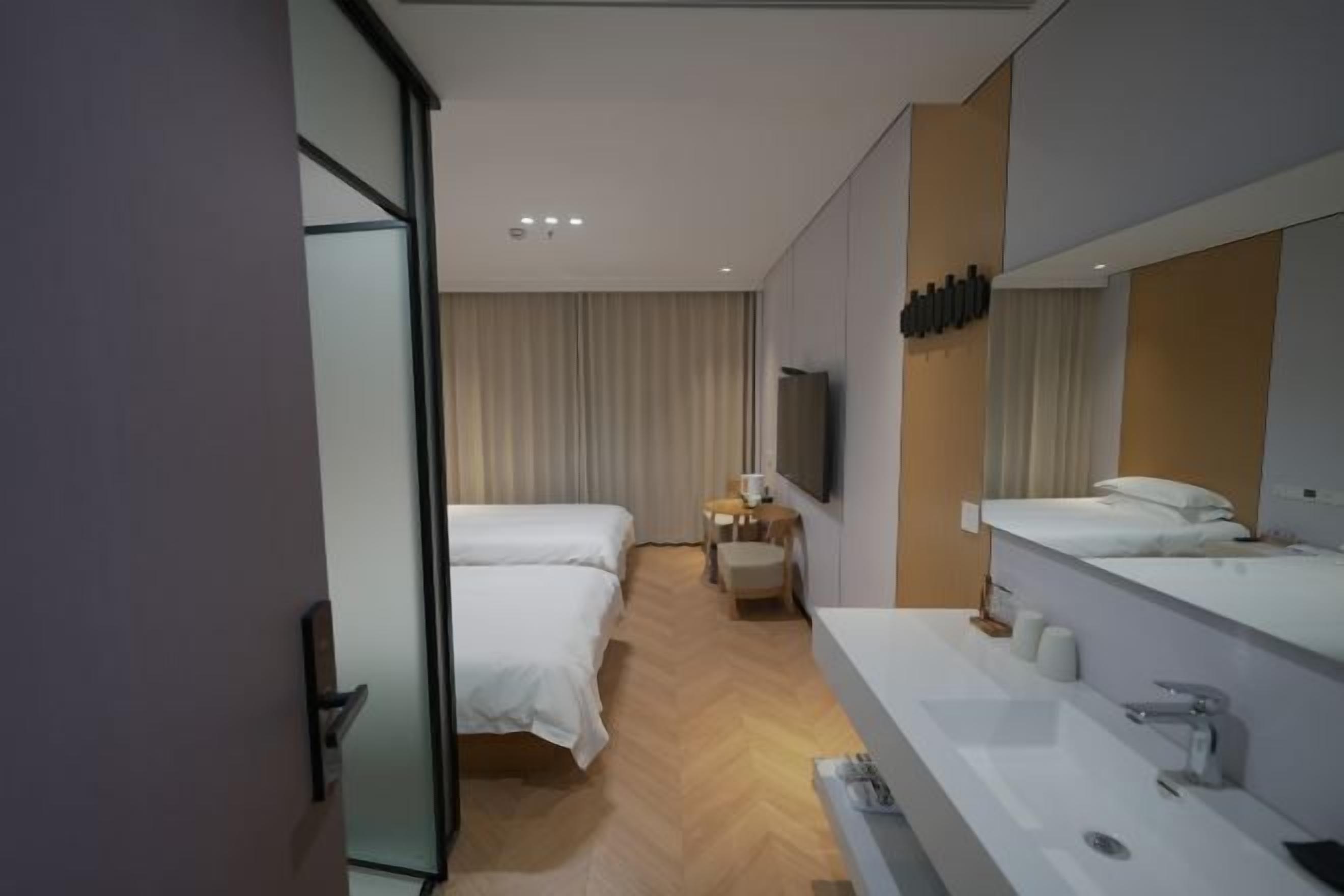 A hotel room with a bed, a bedside table, a TV, a large mirror, and a bathroom with a sink and toilet.