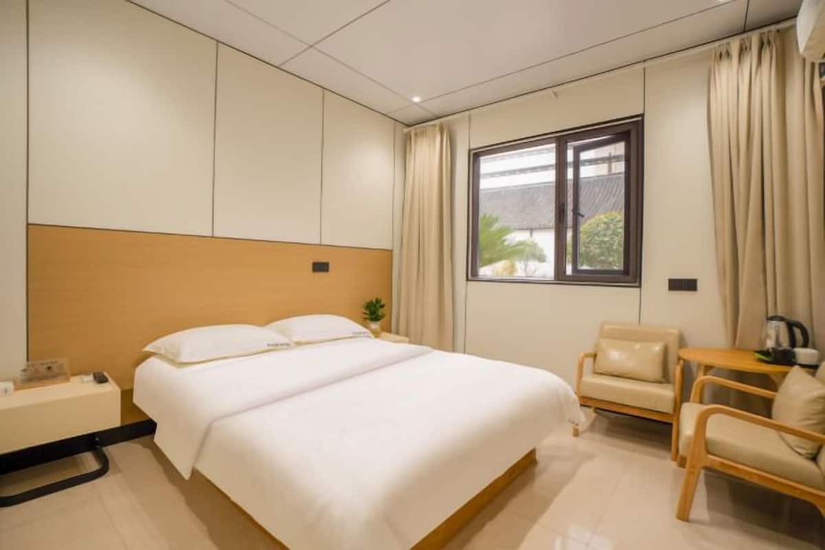 Quarto de hotel com cama, uma cadeira, uma mesa pequena e uma janela.