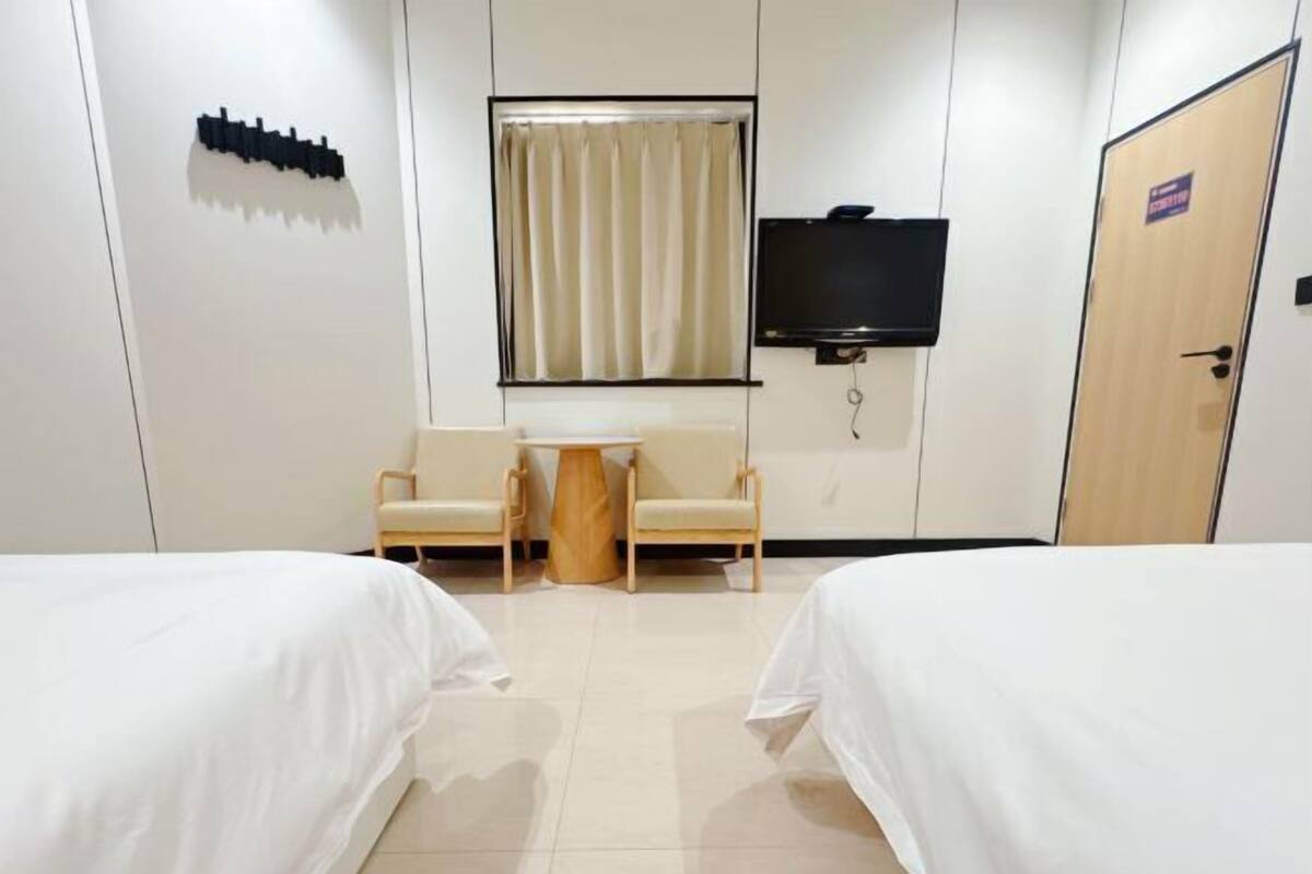 Quarto de hotel com duas camas, uma televisão, uma mesa pequena com cadeiras e uma cortina.