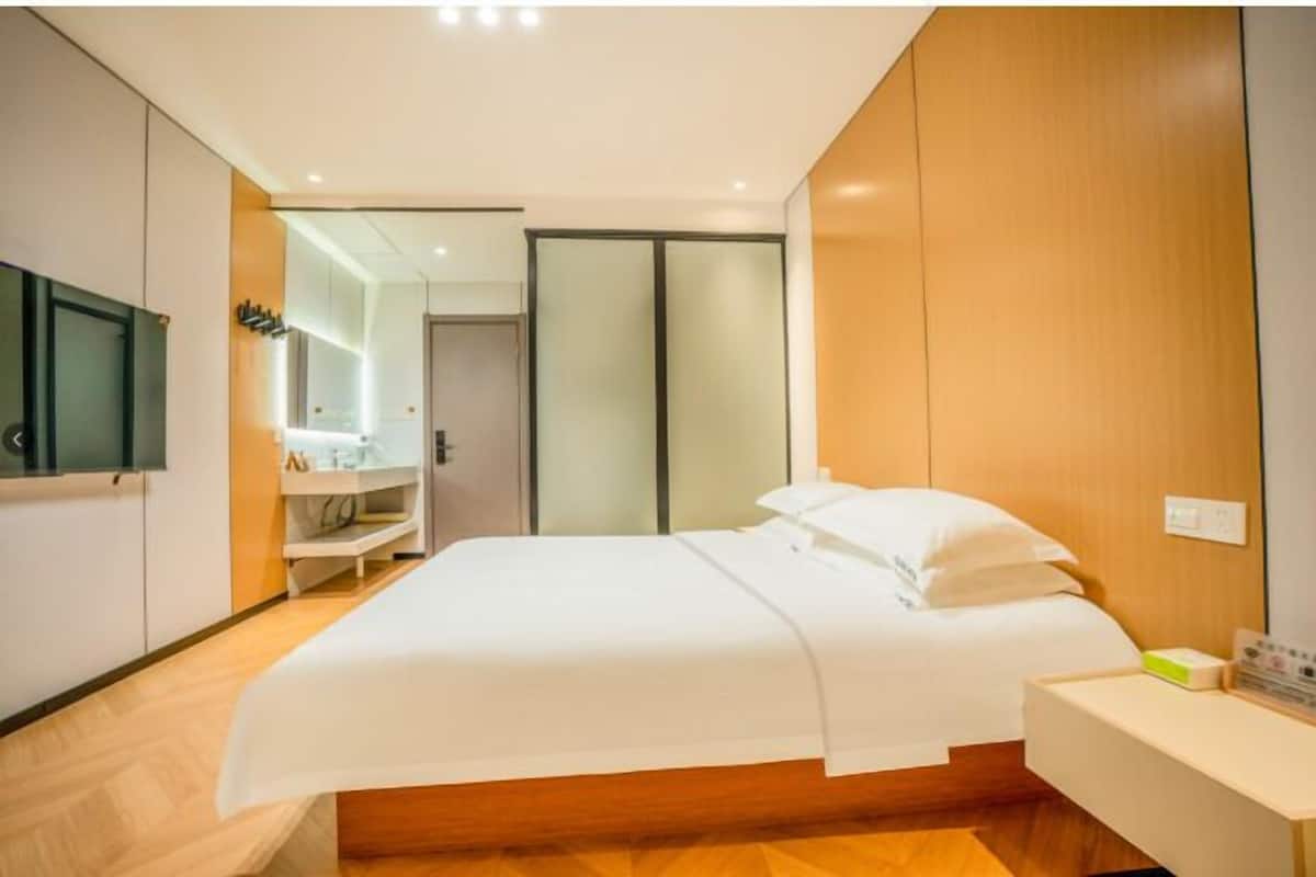 Quarto de hotel moderno com cama, mesa de cabeceira, espelho e guarda-roupa.