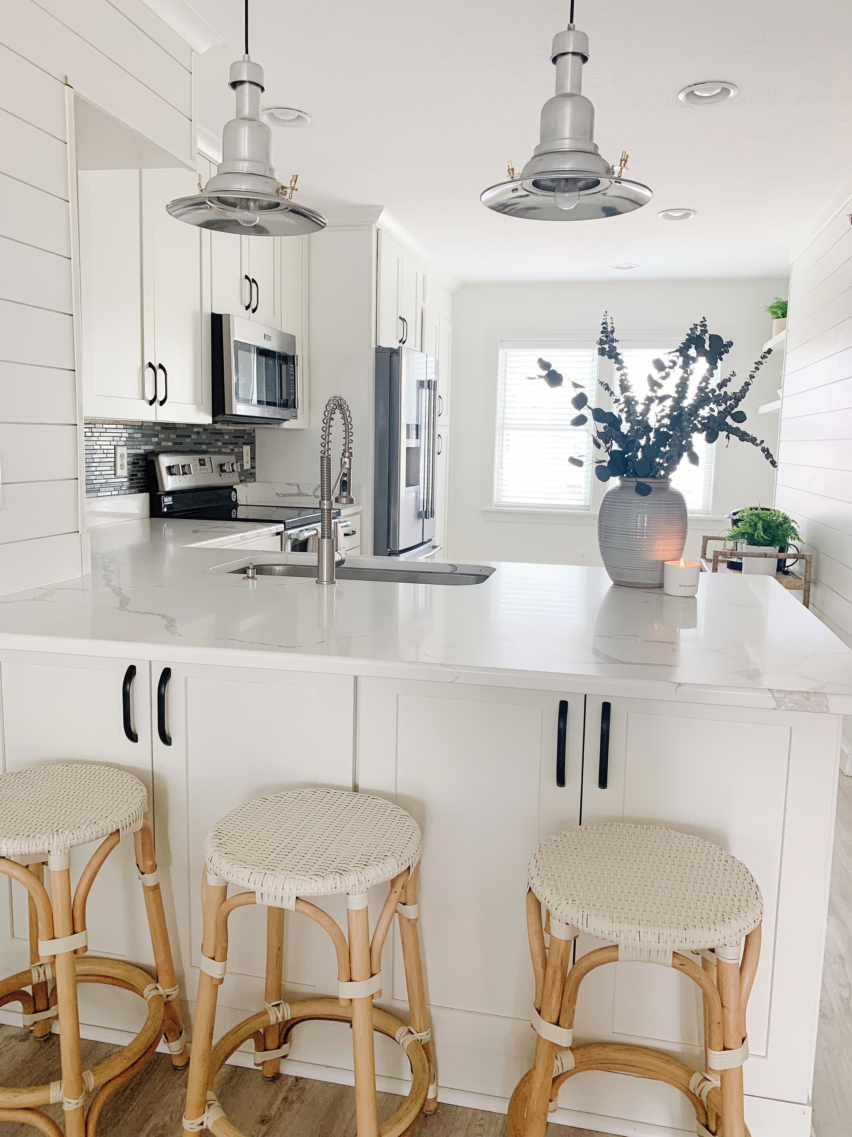 A modern kitchen with white cabinetry, stainless steel appliances, and three wicker bar stools.