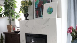 A modern living room with a white fireplace, a white chair, and a dining table with a vase of flowers.