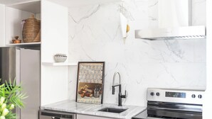 A modern kitchen with white cabinetry, a stainless steel refrigerator, a dishwasher, a sink, and a built-in oven.