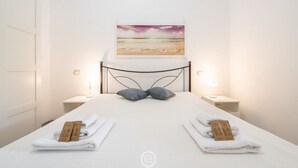 En pænt redt seng med et sengegavl, to natborde med lamper og et billede af en strandscene over sengen.