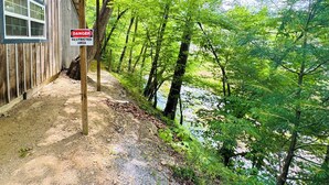 Una cabaña con un cartel de 'DANGER RESTRICTED AREA', rodeada de un bosque denso y un río.